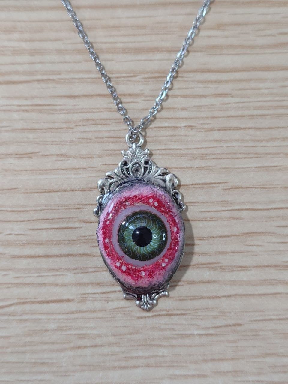 Collar artesanal ovalado con ojo verde y marco plateado, vista frontal